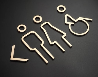 May include: Three wooden signs with outline symbols for men's, women's, and accessible restrooms. The signs are arranged in a row with a left-facing arrow to the left of the men's sign.