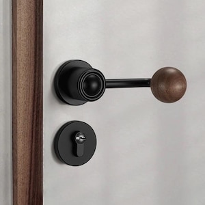 Puede incluir: Pomo de puerta negro con pomo de madera y una cerradura. El pomo está fijado a una puerta blanca.