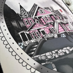 May include: A detailed illustration of a pink Victorian house with a dark gray roof and accents. The artwork is framed with a decorative border and features a gray sky and dark trees in the background. The house has multiple windows and a small red flag.