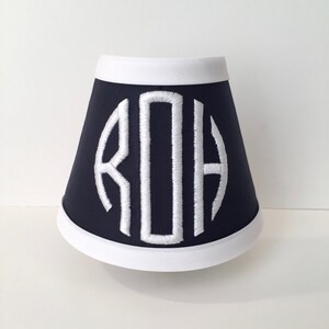 May include: A navy blue lampshade with a white trim and a white embroidered monogram "ROH" in the center.