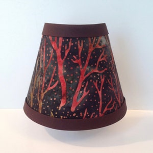 May include: A brown lampshade with a black and red tree pattern. The lampshade has a brown trim around the top and bottom.