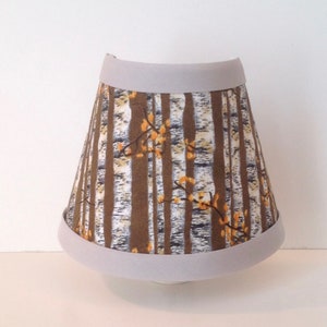 May include: A lampshade with a white trim and a brown and white birch tree pattern.