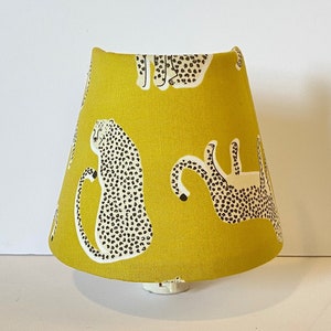 May include: A yellow lampshade with a cheetah print design. The lampshade is made of fabric and has a white trim.