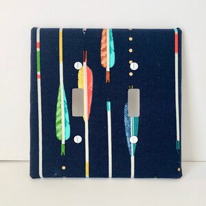 May include: A dark blue double light switch cover with a pattern of colorful arrows and feathers.