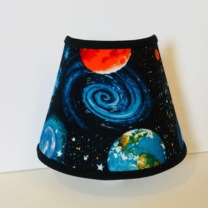 May include: A black lampshade with a space-themed print featuring planets, stars, and a blue nebula. The planets are red, blue, and green.