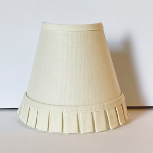 May include: A white lampshade with a pleated ruffle at the bottom.