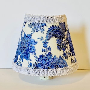 May include: A white lampshade with a blue floral pattern and white trim. The lampshade is made of fabric and has a scalloped edge.