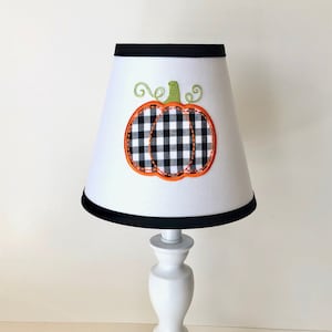 May include: White table lamp with a black and white checkered pumpkin design on the lampshade. The lamp has a white base.