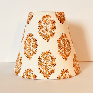May include: A white lampshade with a gold floral pattern. The lampshade is cone-shaped and has a scalloped edge.