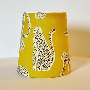 May include: A yellow lampshade with a cheetah print design. The lampshade is made of fabric and has a white background with black cheetah spots.
