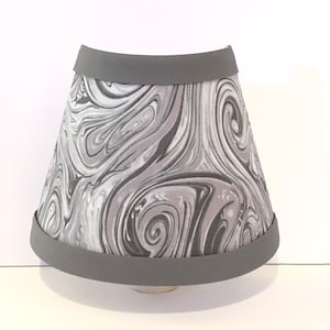May include: A gray lampshade with a swirling black and white marble pattern. The lampshade has a gray fabric trim around the top and bottom.