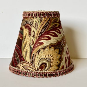 May include: A lampshade with a paisley pattern in shades of brown, red, gold, and green. The lampshade has a gold and red trim.