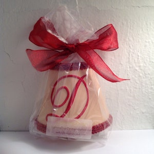 May include: A cream-colored lampshade with a red embroidered letter D. The lampshade is wrapped in clear plastic and tied with a red ribbon.