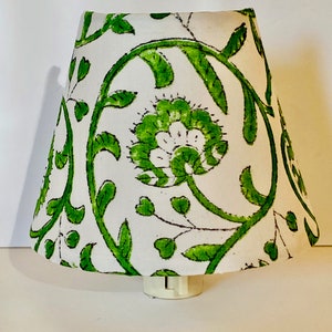 Puede incluir: Una pantalla de l&aacute;mpara blanca con un patr&oacute;n floral verde. La pantalla de la l&aacute;mpara est&aacute; hecha de tela y tiene un borde blanco.