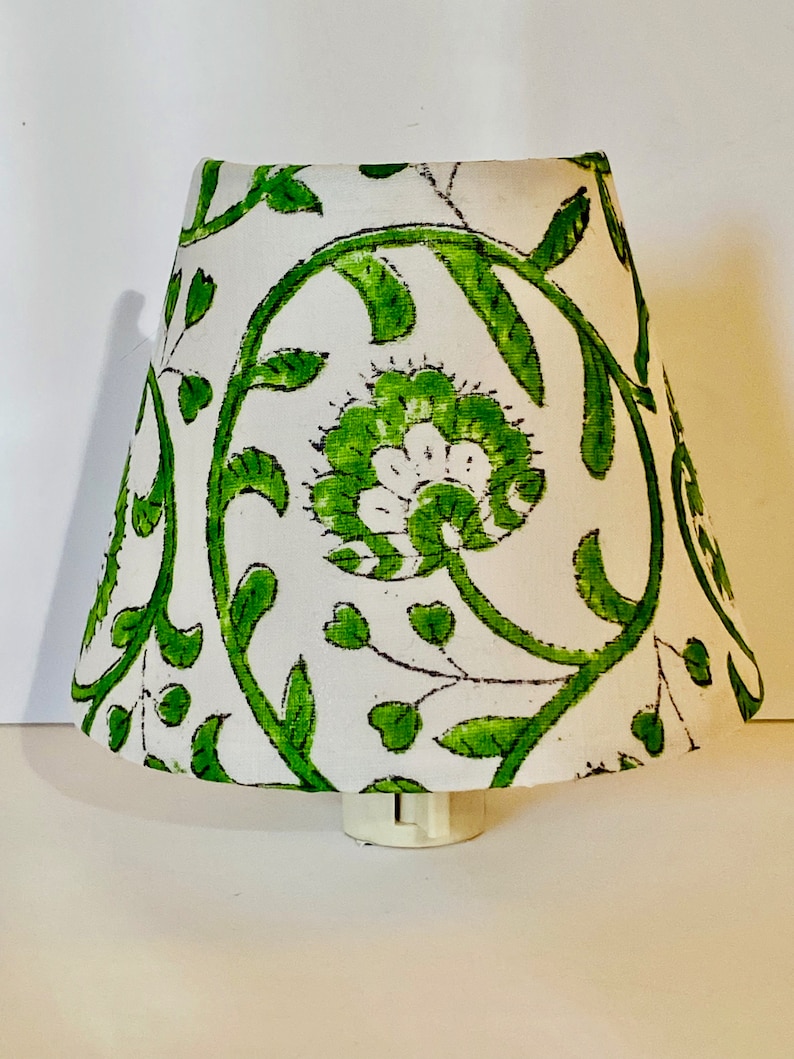 Puede incluir: Una pantalla de l&aacute;mpara blanca con un patr&oacute;n floral verde. La pantalla de la l&aacute;mpara est&aacute; hecha de tela y tiene un borde blanco.