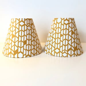 May include: Two lampshades with a geometric pattern in white on a mustard yellow background.