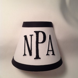 May include: White lampshade with a black trim and the letters "NPA" embroidered in black.