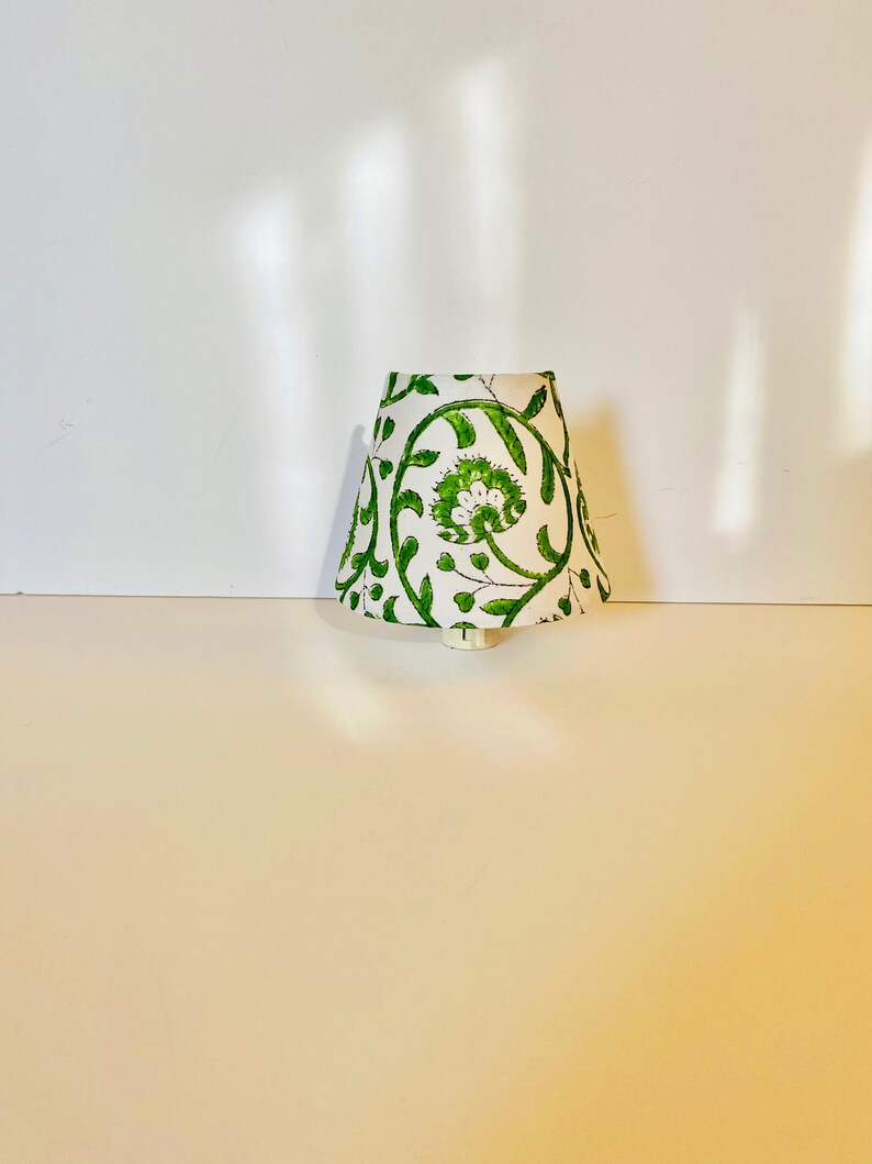 Puede incluir: Una pantalla de l&aacute;mpara con estampado floral blanco y verde con un enchufe blanco.