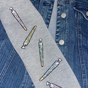 May include: A gray sweatshirt with a denim jacket. The sweatshirt has four embroidered images of colorful joints with smiley faces on them.
