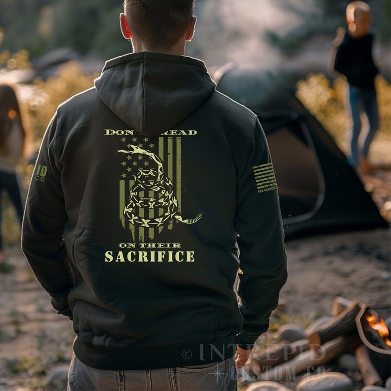May include: A dark green hooded sweatshirt with a graphic of a coiled snake over an American flag design. The text "DON'T TREAD ON THEIR SACRIFICE" is printed on the back. The sweatshirt has a hood and a kangaroo pocket.