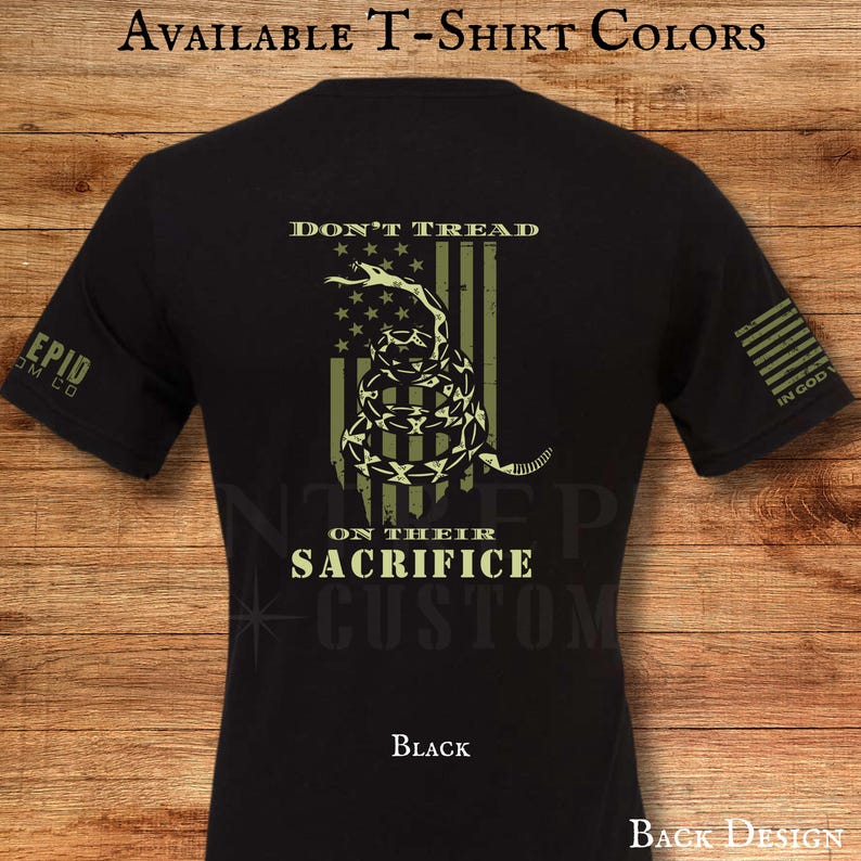 May include: Black t-shirt with a distressed design featuring a coiled snake, stars, and stripes, with the words "DON'T TREAD" and "ON THEIR SACRIFICE". The shirt also has the text "EPID OM CO" on the sleeve.