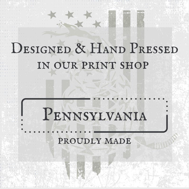 May include: A light gray graphic with the text "Designed & Hand Pressed in Our Print Shop" above a rectangular box with the word "Pennsylvania" inside. The words "Proudly Made" are below the box. The background has a distressed look.