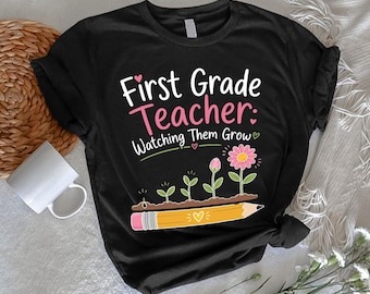 May include: A black short-sleeved t-shirt featuring the white and pink text First Grade Teacher: Watching Them Grow. The graphic includes a yellow pencil base with small green sprouts and a pink flower growing from it, accented by tiny hearts.