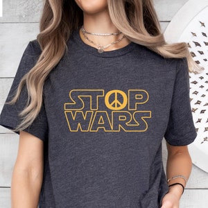 May include: A dark gray t-shirt with the text "STOP WARS" in yellow with a peace sign in the middle of the word "STOP".