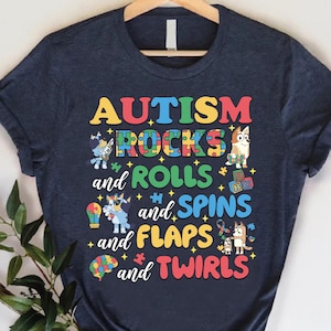 May include: A dark blue t-shirt with the text "AUTISM ROCKS and ROLLS and SPINS and FLAPS and TWIRLS" in colorful letters. The text is surrounded by colorful puzzle pieces and cartoon animals.