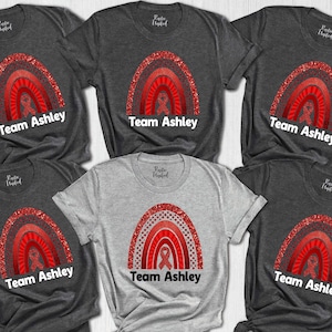 May include: Six t-shirts with a red glitter rainbow design and the text "Team Ashley". The t-shirts are in various shades of gray.