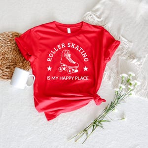 May include: A red t-shirt with the text "ROLLER SKATING IS MY HAPPY PLACE" in white. The design includes a roller skate graphic and two stars. The shirt is knotted at the bottom.