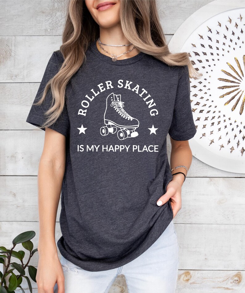May include: Dark gray t-shirt with the text "ROLLER SKATING IS MY HAPPY PLACE" in white. The design features a roller skate illustration with stars. The shirt is a crew neck and has short sleeves.