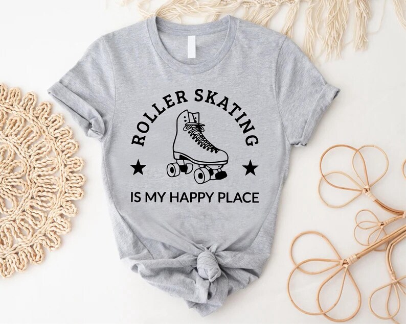 May include: A light gray t-shirt with a black graphic that says "ROLLER SKATING IS MY HAPPY PLACE." The graphic features a roller skate and two stars. The shirt is tied in a knot at the bottom.