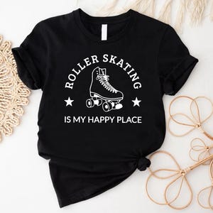 May include: Black t-shirt with a white graphic that reads "ROLLER SKATING IS MY HAPPY PLACE." The design features a roller skate and two stars. The shirt is made of a soft material and has short sleeves.