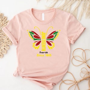 May include: Pink t-shirt with a yellow butterfly graphic. The butterfly has red, green, and black wings. The text "Juneteenth" is written vertically down the butterfly's body. The text "Free-ish Since 1865" is written below the butterfly.