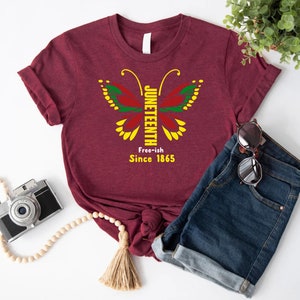 May include: A maroon t-shirt with a butterfly design featuring the words "Juneteenth Free-ish Since 1865".