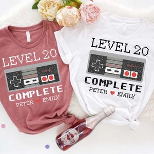 May include: Two t-shirts with a video game controller graphic and the text "Level 20 Complete" with names "Peter" and "Emily".