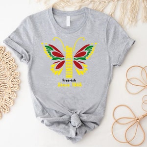 May include: Gray t-shirt with a butterfly design featuring the words "Juneteenth" and "Free-ish Since 1865".