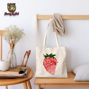 May include: A white canvas tote bag with a red and green strawberry design. The strawberry is made up of the words "Strawberry Fields Forever".