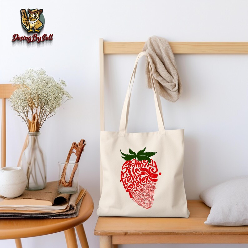 May include: A white canvas tote bag with a red and green strawberry design. The strawberry is made up of the words "Strawberry Fields Forever".