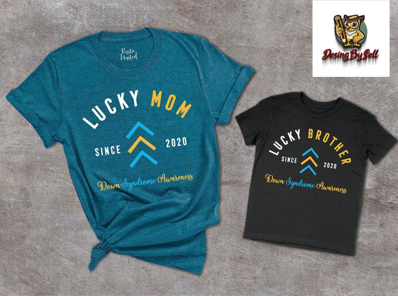 Op de afbeelding: Twee T-shirts, een tealblauw en een zwart, met de tekst "Lucky Mom" en "Lucky Brother" in wit. Beide shirts hebben een geel en blauw naar boven wijzend pijlontwerp en de tekst "Since 2020" en "Down Syndrome Awareness".