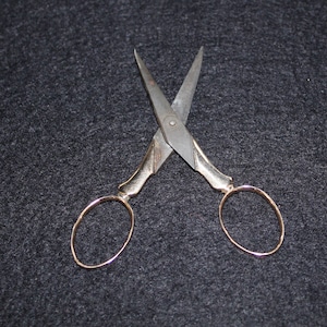 May include: A pair of antique silver-toned scissors with gold-colored handles. The scissors are open and the blades are crossed.