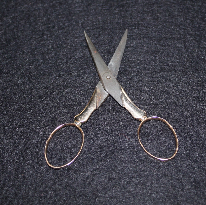 May include: A pair of antique silver-toned scissors with gold-colored handles. The scissors are open and the blades are crossed.