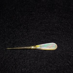 May include: A gold and iridescent mother-of-pearl handled tool with a sharp point.