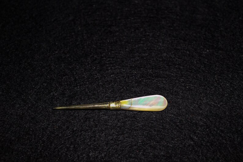 May include: A gold and iridescent mother-of-pearl handled tool with a sharp point.