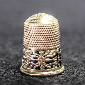 May include: A silver thimble with a black and gold floral design around the base.