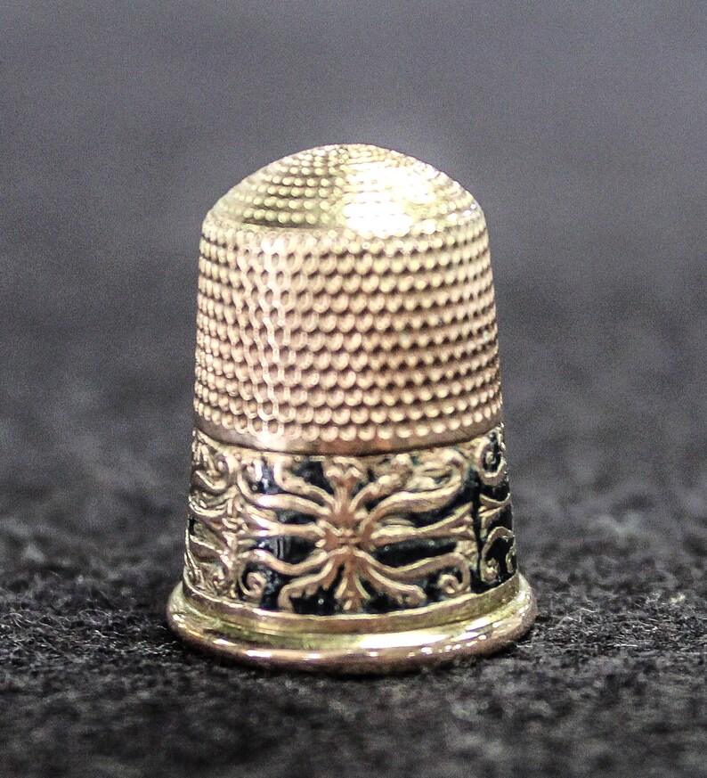 May include: A silver thimble with a black and gold floral design around the base.