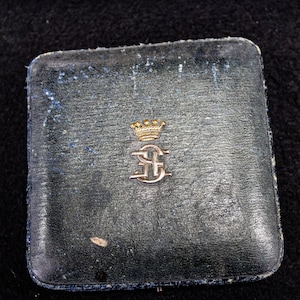 May include: A black leather box with a gold crown and initials "E.C." embossed on the lid.