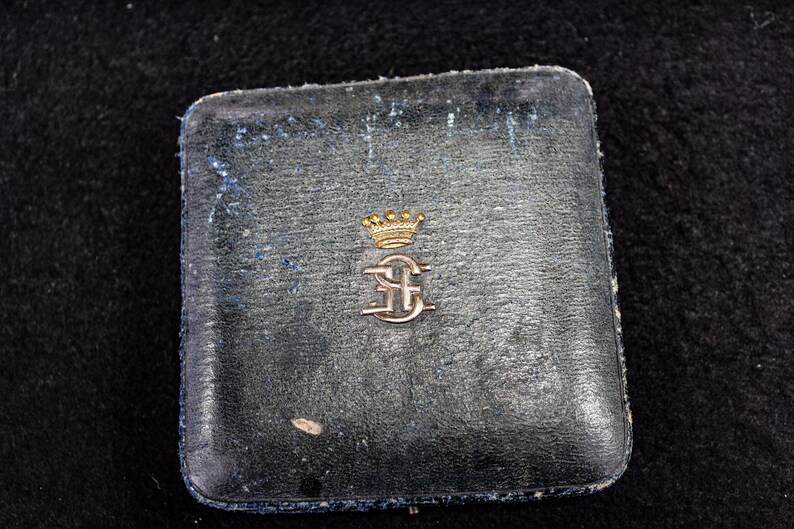 May include: A black leather box with a gold crown and initials "E.C." embossed on the lid.