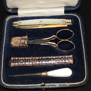 May include: A vintage sewing kit in a blue velvet box. The kit includes a pair of gold-plated scissors, a thimble, a needle case, and a small knife with a pearl handle.